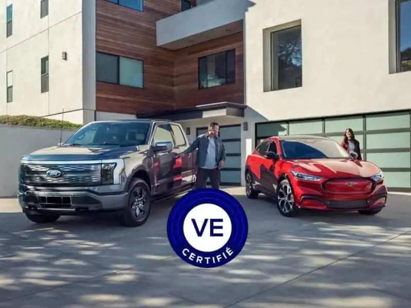 Deux véhicules électriques Ford, un pick-up gris et une berline rouge, sont présentés devant une maison moderne. Un homme et une femme se tiennent à côté des voitures, mettant en avant la certification VE.
