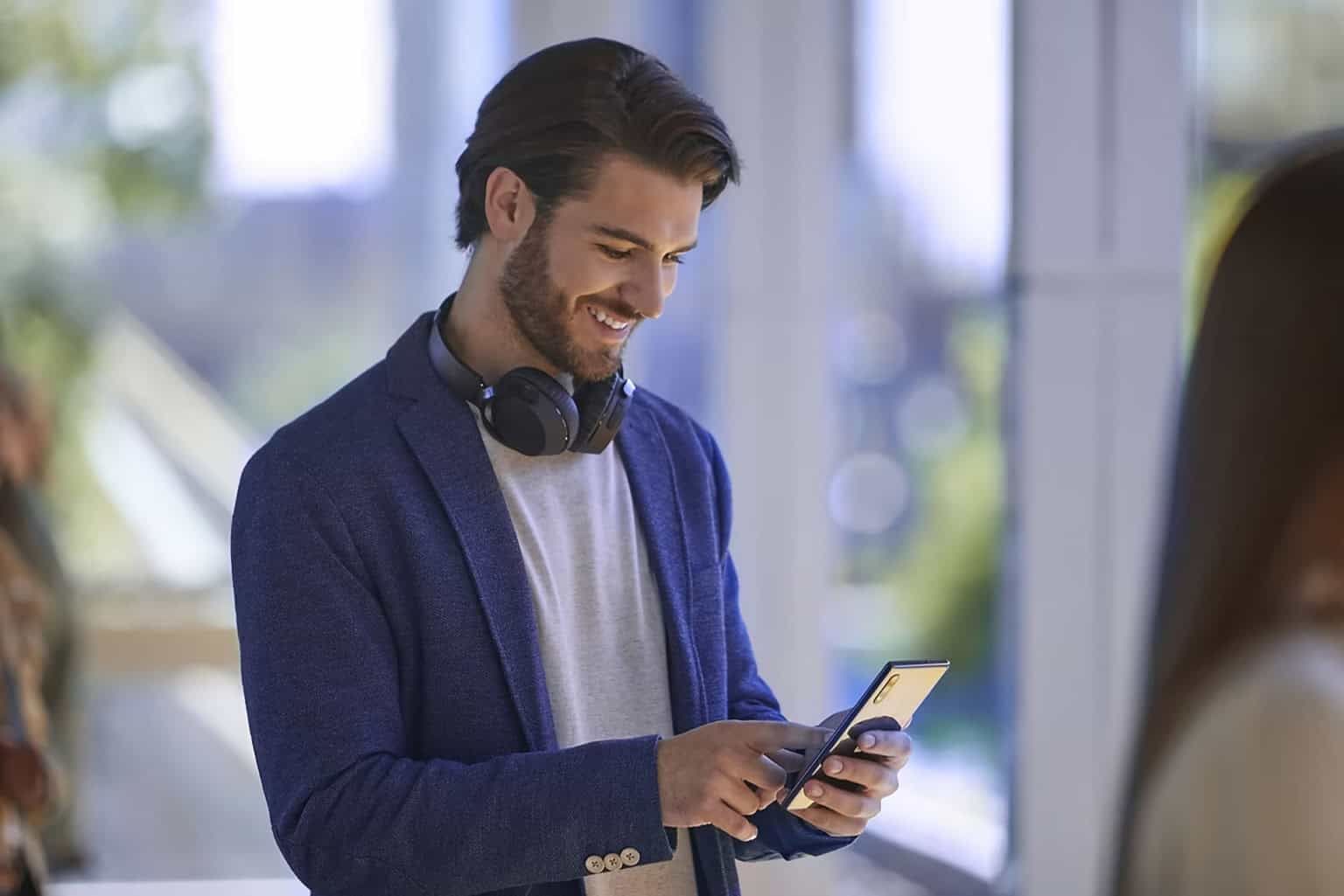 Homme souriant avec des écouteurs regardant un smartphone dans un cadre lumineux et moderne.